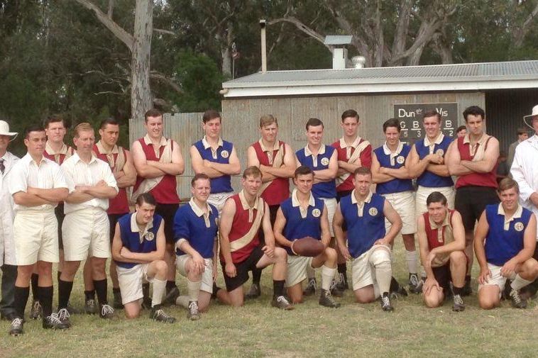 Some of the Dungatar (in red and white) and Winyerp (in blue) players pose with the game's umpires in front of the unaccounted-for scoreboard.